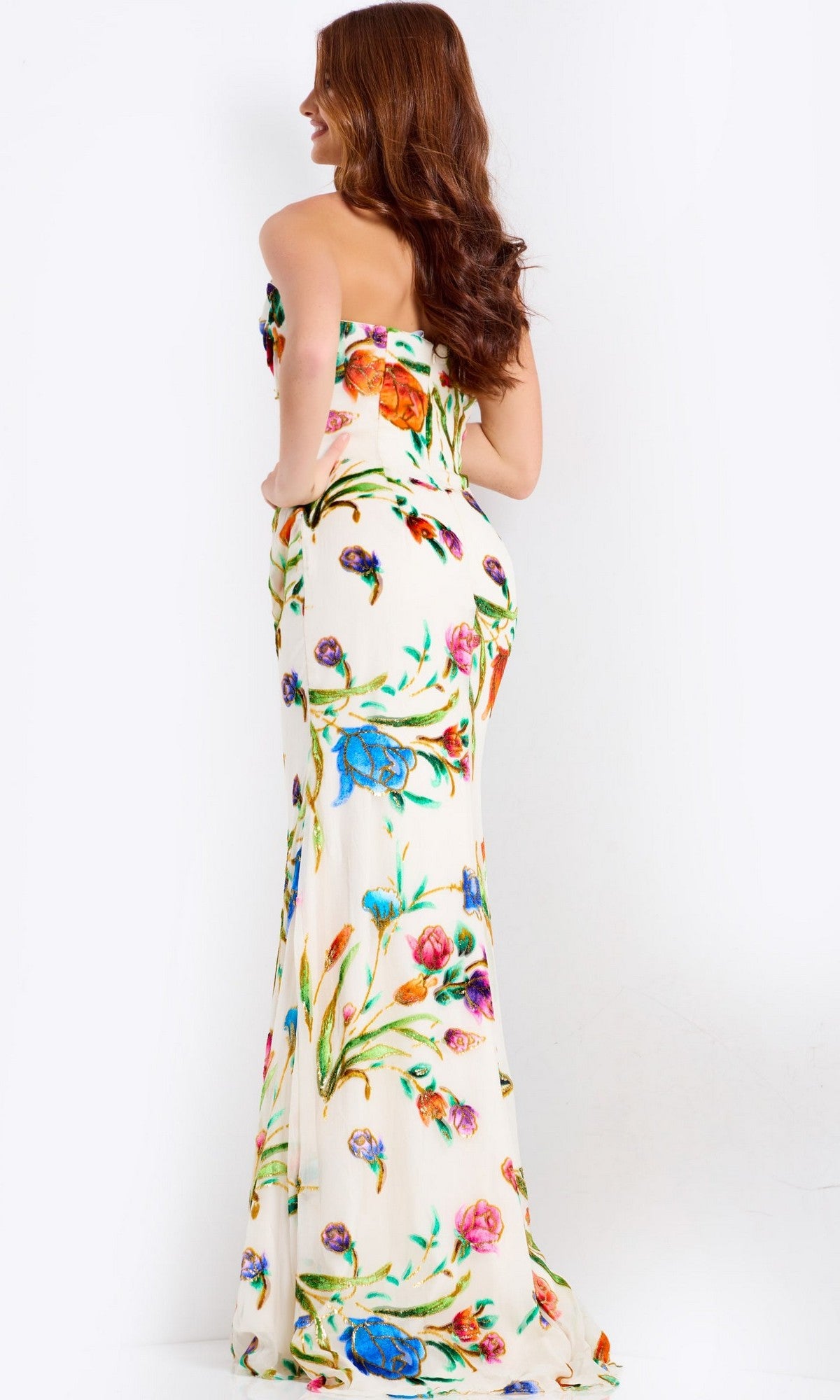 A woman with long brown hair models the Jovani 47626, a strapless floor-length prom dress with a floral design, while standing facing away from the camera against a plain white background.